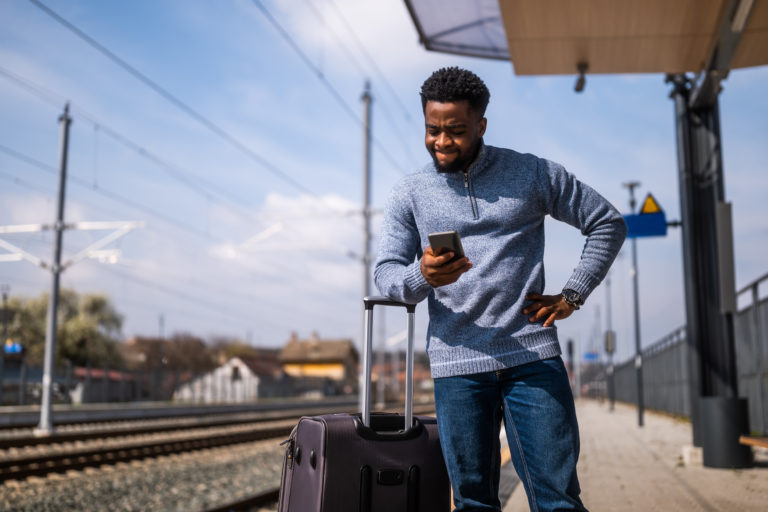 Angry man with a suitcase and mobile phone standing on a railway station.
